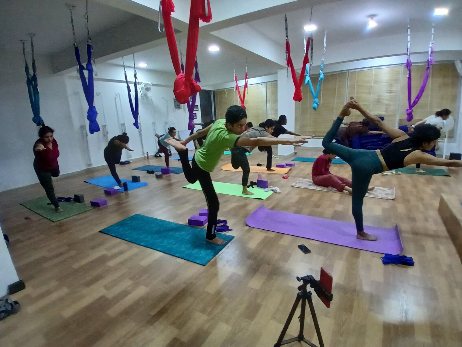 A full class at Manas.Fit practising Natarajasana beneath aerial hammocks